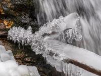 Glitzernde Eisfiguren an Ast bei Kaskade im Steinbach